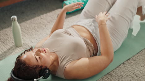 woman lying on a yoga mat meditating with headphones