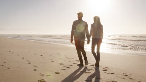 rear view of loving couple walking along winter beach together