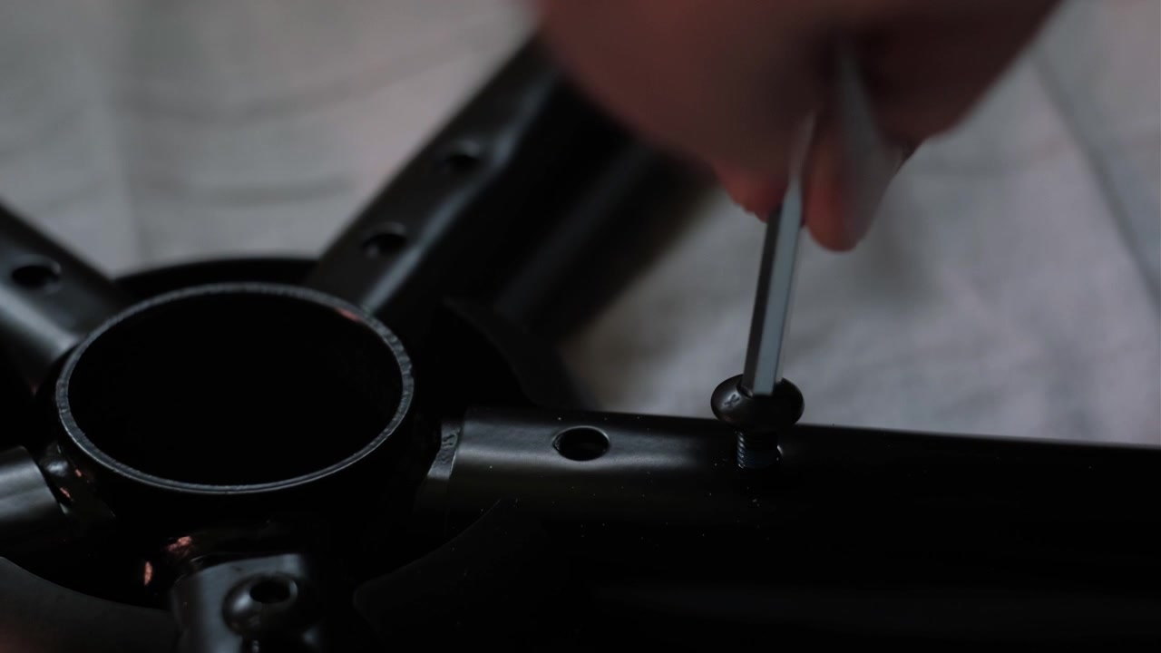 Close-up de mãos apertando a base de uma cadeira gamer com uma chave Allen durante a montagem de móveis em baixa luminosidade