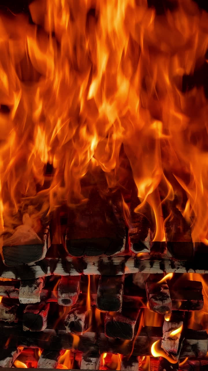 Logs carefully stacked in a pile burn with good flame. Wood burning for barbeque. Close up. Vertical video.