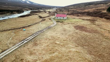 a drone flys towards a the recently renovated red house bothy in the scottish highlands as a person walks out of the front door