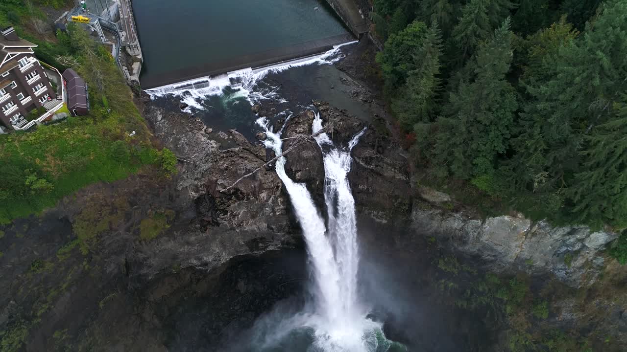 antena alejándose de las cataratas de snoqualmie para revelar un denso bosque y un albergue para visitantes