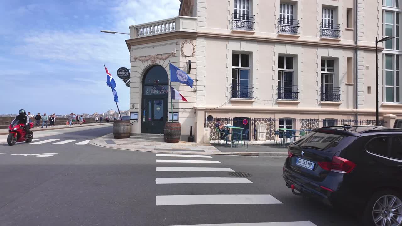 Crossing the street with flags are waving on the hotel building opposite coastal promenade, Saint Malo, France