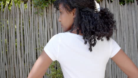 rear view of biracial woman with long hair in white t shirt with hands on hips outdoors, slow motion