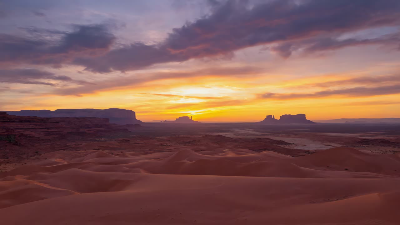 Dramatic Sunset Over a Vast Desert Landscape with Buttes and Sand Dunes