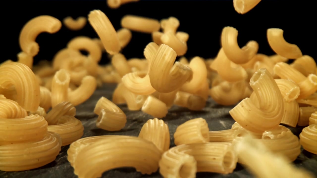 Pasta maccheroni secca che cade al rallentatore su sfondo nero.