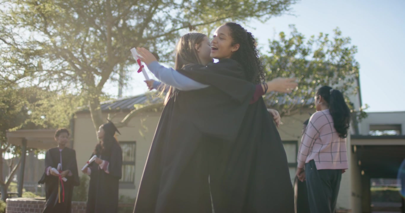 Donne indiane e africane in toga che alzano il braccio lanciando i toques con i diplomi, abbracciandosi e festeggiando nel campus.