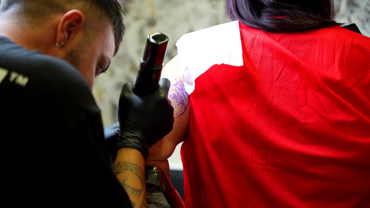 Tatuatore che lavora meticolosamente al tatuaggio sul braccio superiore del cliente durante una sessione in studio