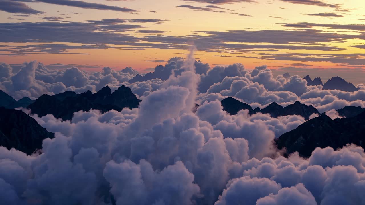 Aerial video view of dramatic clouds over jagged mountain peaks at sunset, capturing a serene
