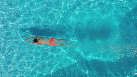 Drohnenaufnahme-über-Dem-Kopf-Eines-Mannes,-Der-In-Ein-Freibad-Taucht-Und-Unter-Wasser-Schwimmt