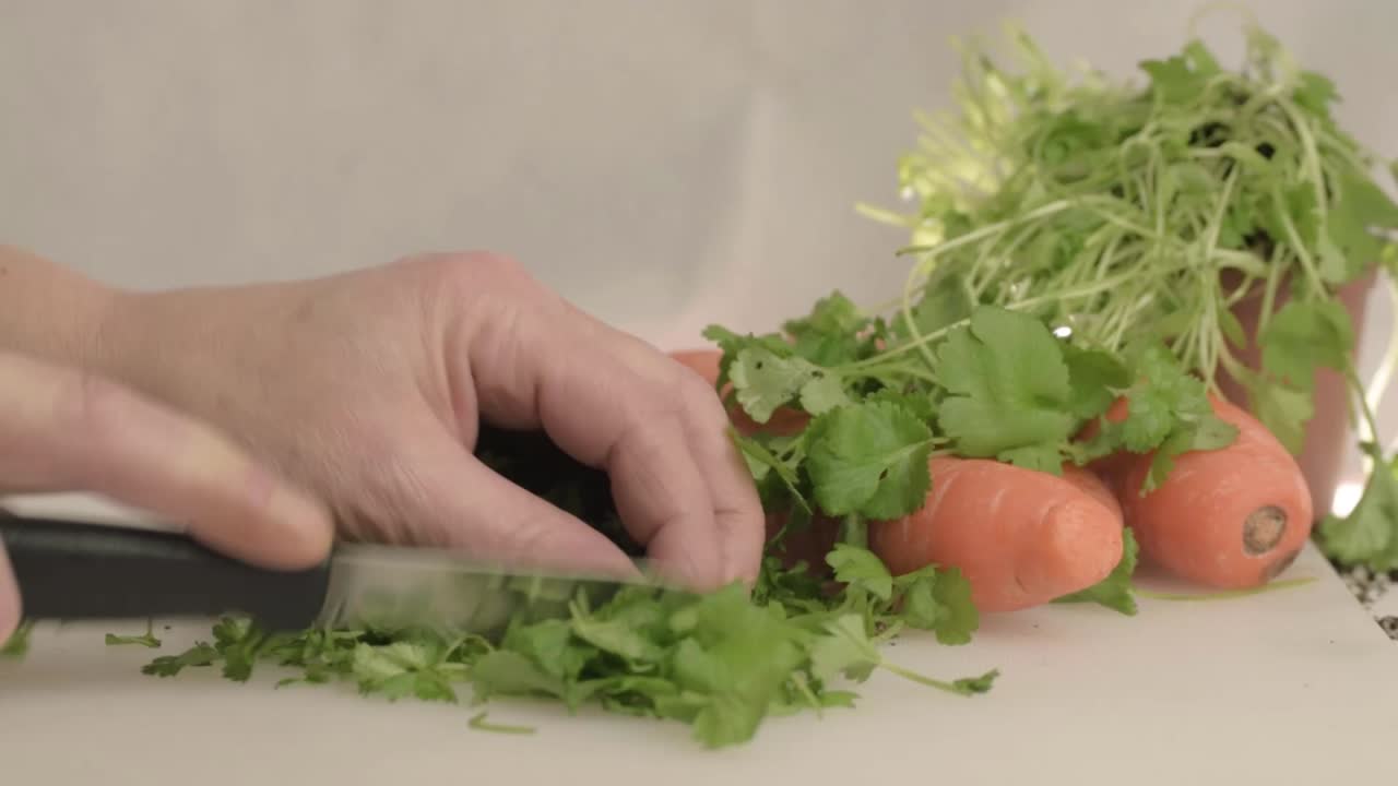 Hands cutting fresh coriander herb in kitchen with carrots wide shot