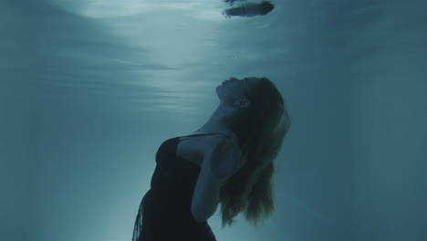 woman with red hair poring in a black dress underwater