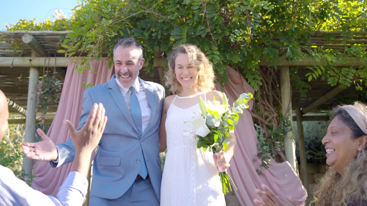 Paar loopt met opgeheven armen nadat de ambtenaar het huwelijk heeft voltrokken, gasten klappen en feliciteren.