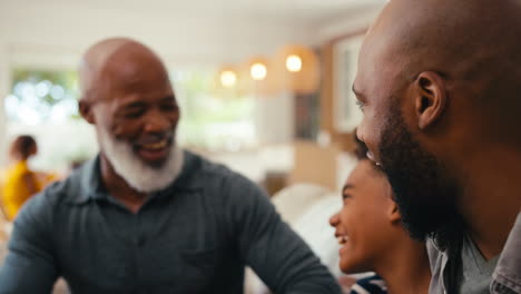 Cerca-De-Una-Familia-Masculina-Multigeneracional-Riéndose-Sentada-En-El-Sofá-De-Casa-Hablando-Juntos