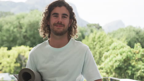 young caucasian man smiles outdoors, holding a yoga mat