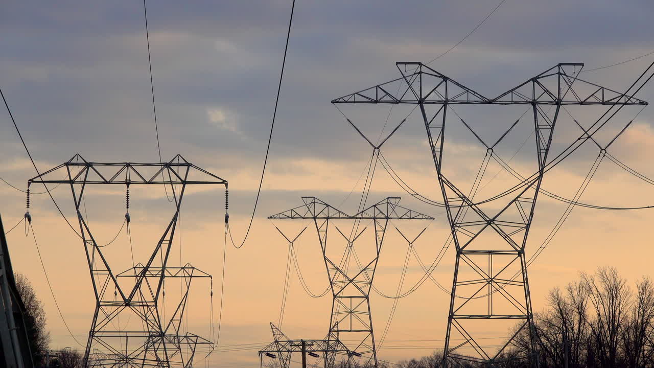 Telephoto shot of multiple electricity towers against cloudy sky at sunset