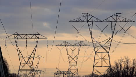 Telephoto-shot-of-multiple-electricity-towers-against-cloudy-sky-at-sunset