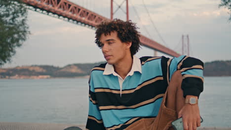 Travel-guy-resting-embankment-at-Lisbon-zoom-on.-Curly-hair-teen-looking-camera