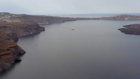 Aerial:-a-ferry-boat-sailing-at-calm-water-of-the-port-of-Santorini,-Greece-during-sunrise