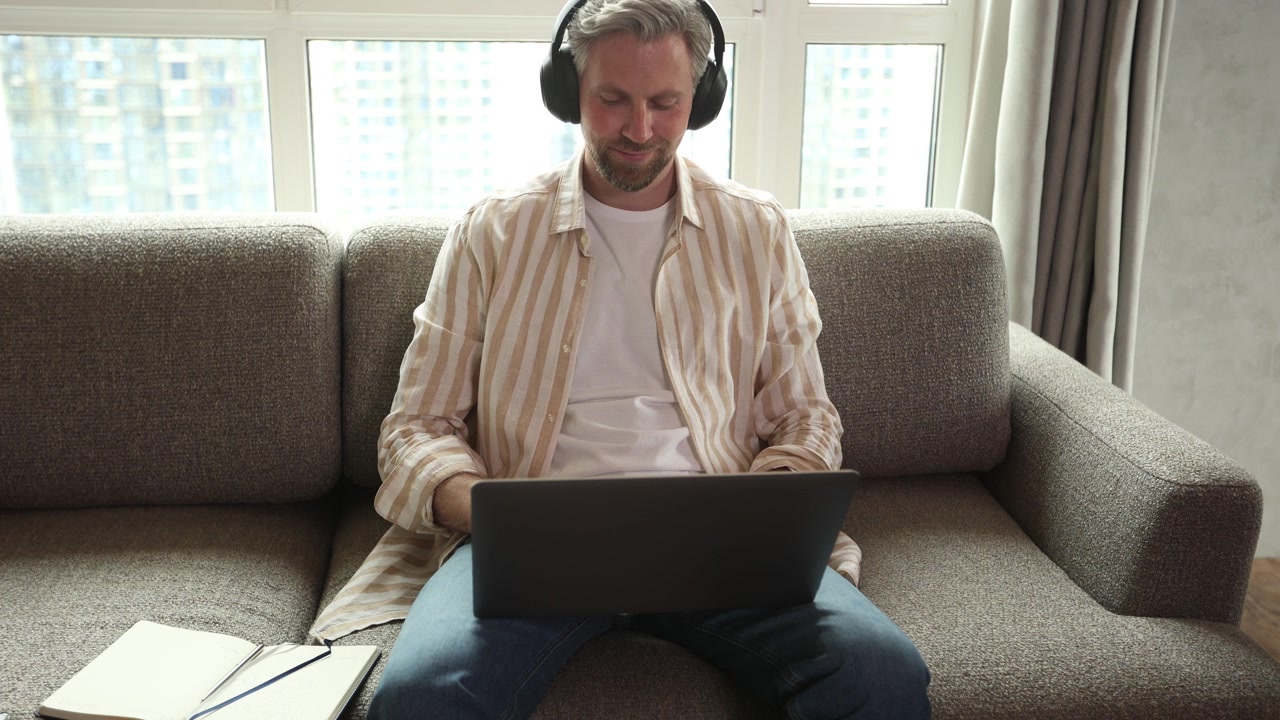 Smiling Man Wearing Headphones Using Laptop at Home