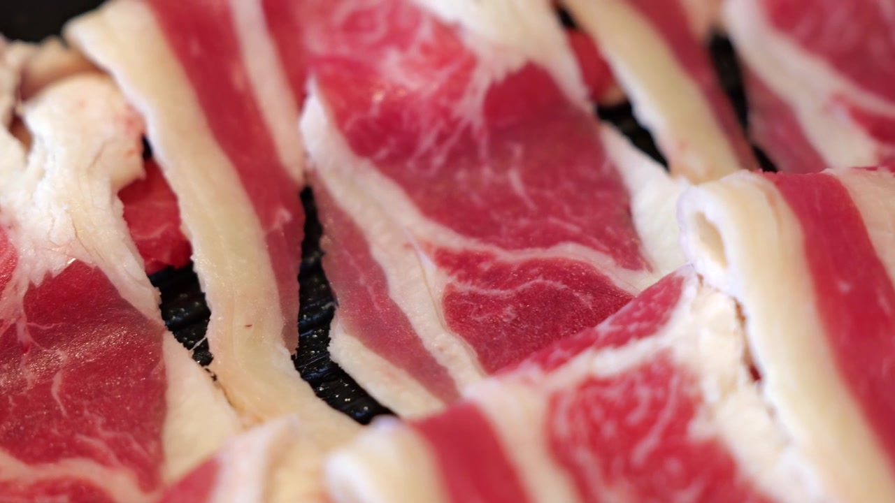Primo piano di carne di manzo cruda tagliata finemente e disposta ordinatamente su un piatto, preparata per la grigliata in stile barbecue thailandese hot pot con marezzatura visibile e consistenza fresca