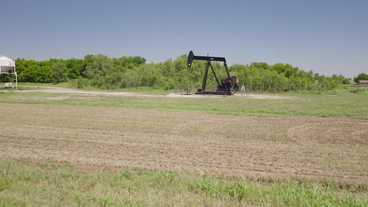 Drone 4K of a field of hay bails surrounding an oil pump jack in the spring and summer.