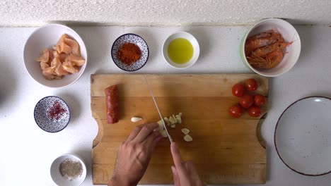 Von-Oben-Nach-Unten-Aussehender-Schuss-Von-Männlichen-Händen,-Die-Knoblauch-Auf-Einem-Holzschneidebrett-In-Der-Küche-Schneiden