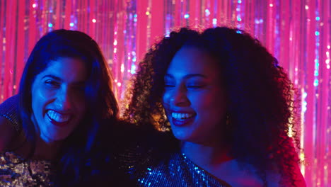 portrait of two women friends having fun dancing in nightclub bar or disco with sparkling lights