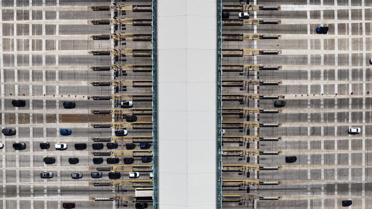 Overhead drone view showing cars queuing and driving through a busy toll plaza on a multi-lane highway, representing transportation infrastructure, commuting, and modern road systems
