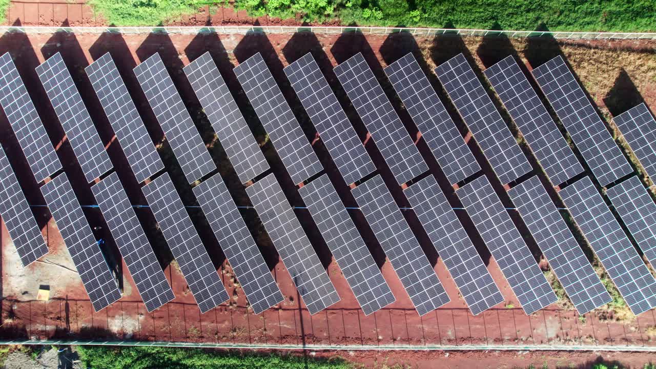 Zoom zenitale su pannelli solari allineati installati su terreno rosso, che mostra motivi geometrici e infrastrutture di energia rinnovabile