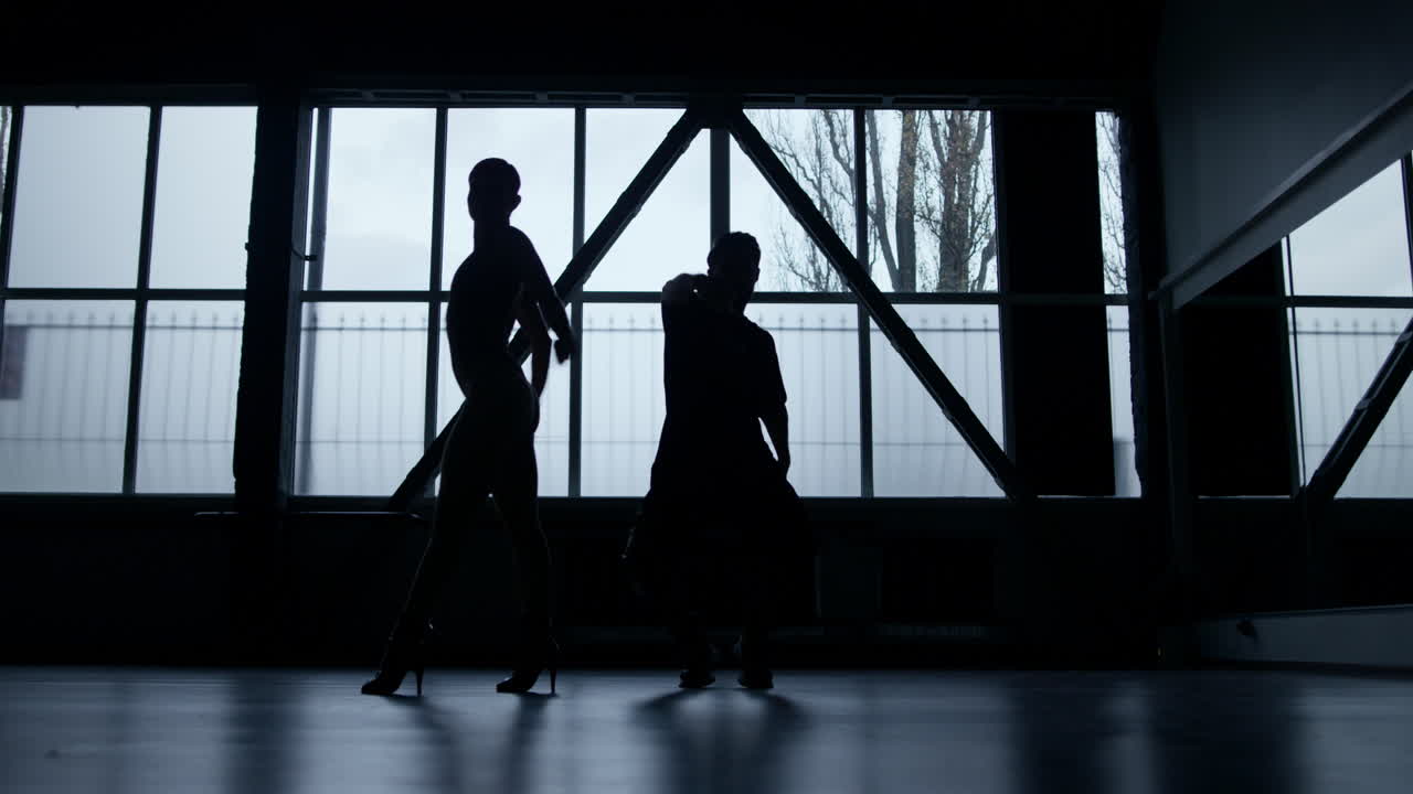 Bailarines en silueta bailando hip hop en un estudio oscuro. Chico y chica bailando.