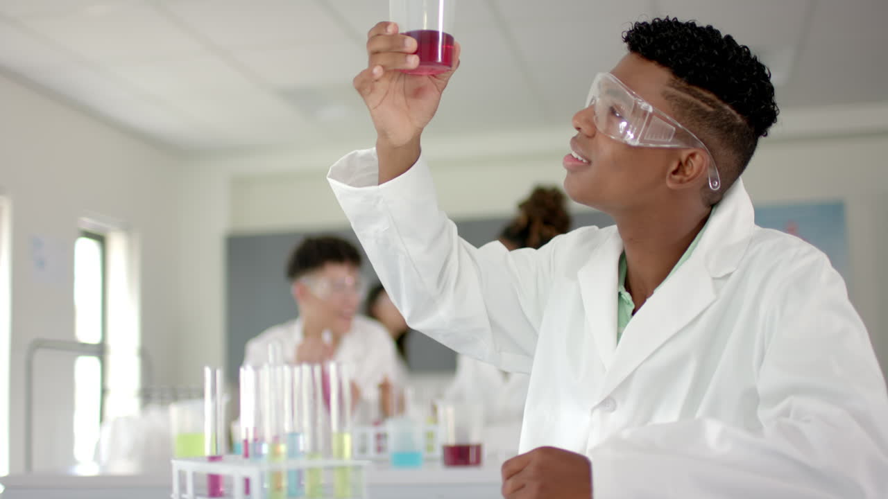 Teenage biracial boy examines a test tube in a high school lab
