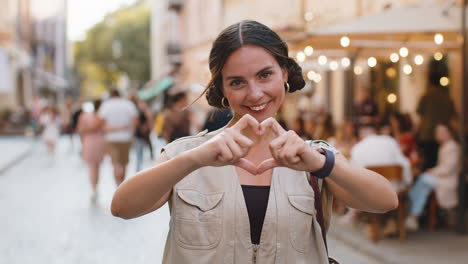 mujer joven hace símbolo de amor, mostrando el corazón señal a la cámara, expresar sentimientos románticos positivos