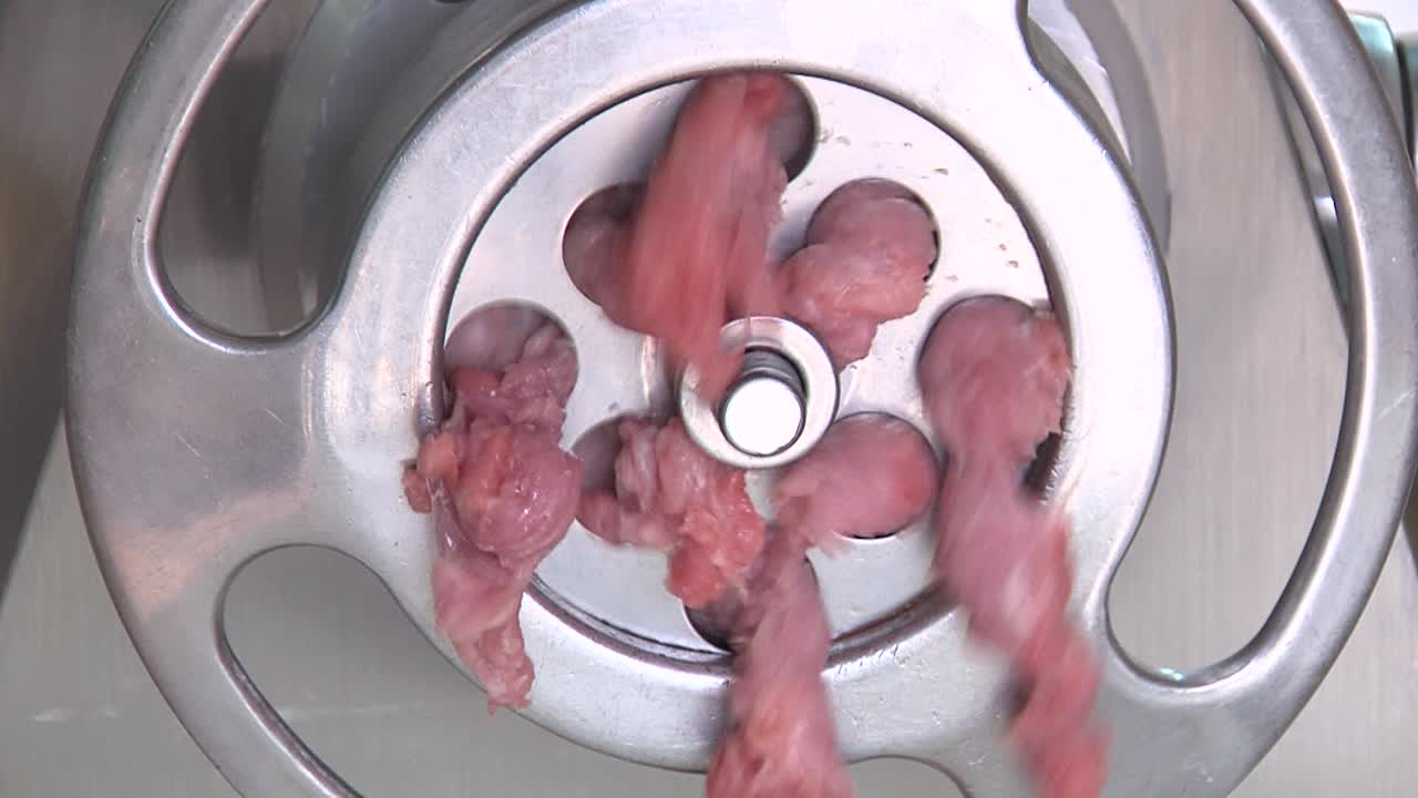 Frontal closeup of raw minced meat pieces coming out of metal meat grinder