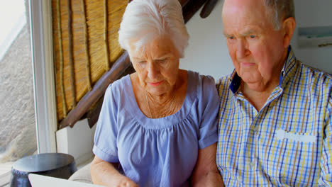 vista frontal de una pareja de ancianos caucásicos usando una computadora portátil en una casa cómoda 4k
