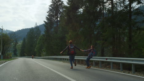 couple run mountain countryside on roadside. smiling hikers hold hands in forest