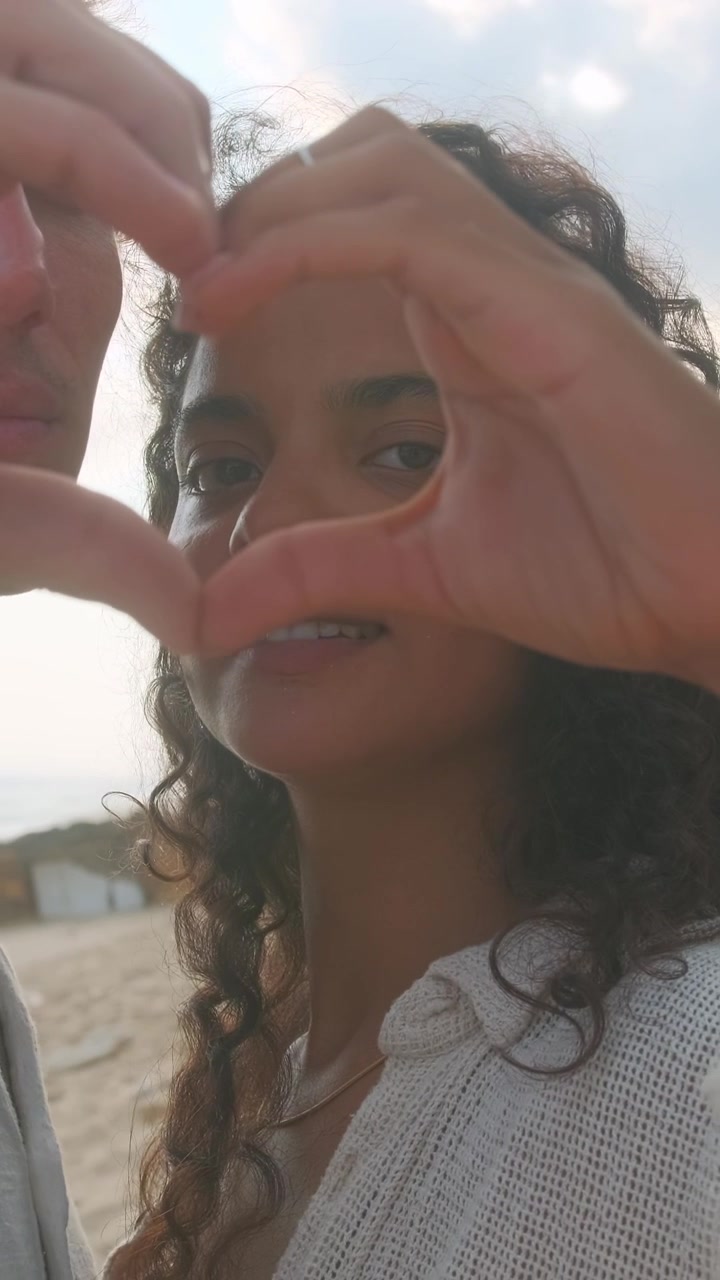Coppia che forma un cuore con le mani stando in piedi sulla spiaggia