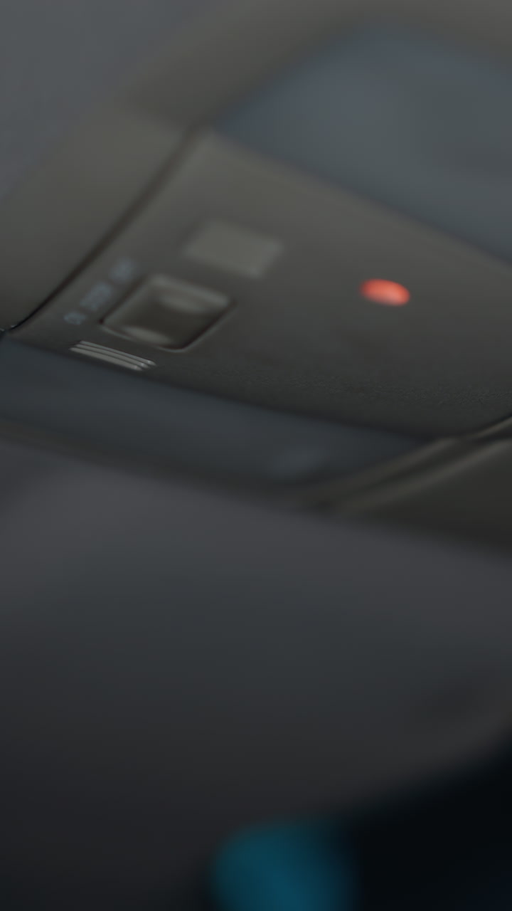 View of a woman turning on the car roof light and reaching for her glasses at night. The scene captures the moment her hand with black painted nails interacts with the car's interior light