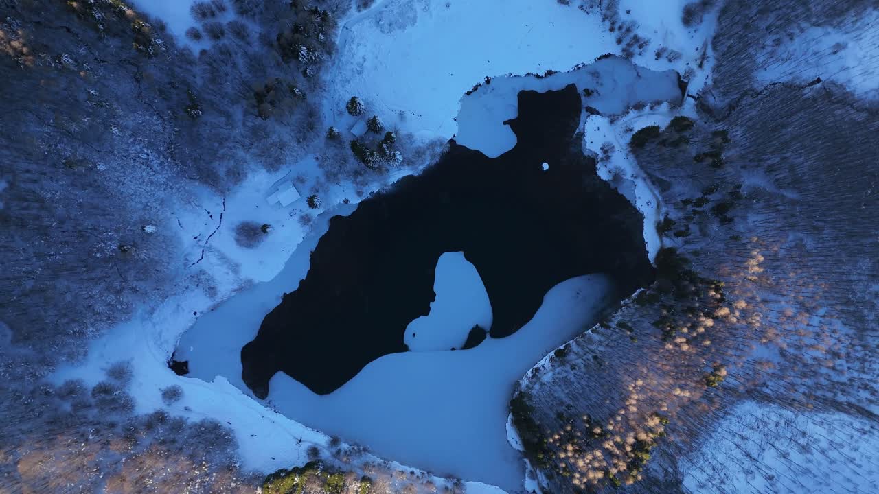 İtalya, Toskana Emilia Apeninleri'nde donmuş bir göl üzerinde, buz oluşumlarını, karla kaplı ormanı ve kış dokularını gösteren zenital spiral uzaklaştırma