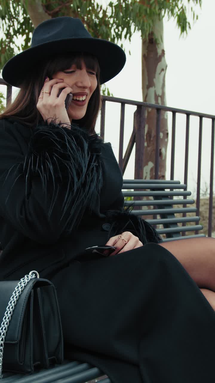 Elegant Woman Dressed In Black Coat Having A Call With A Friend On Town Bench