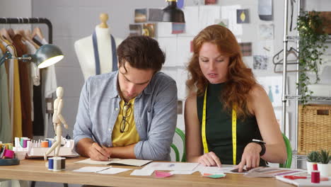 diseñadores de ropa masculinos y femeninos mirando bocetos y trabajando en diseños en un estudio de moda