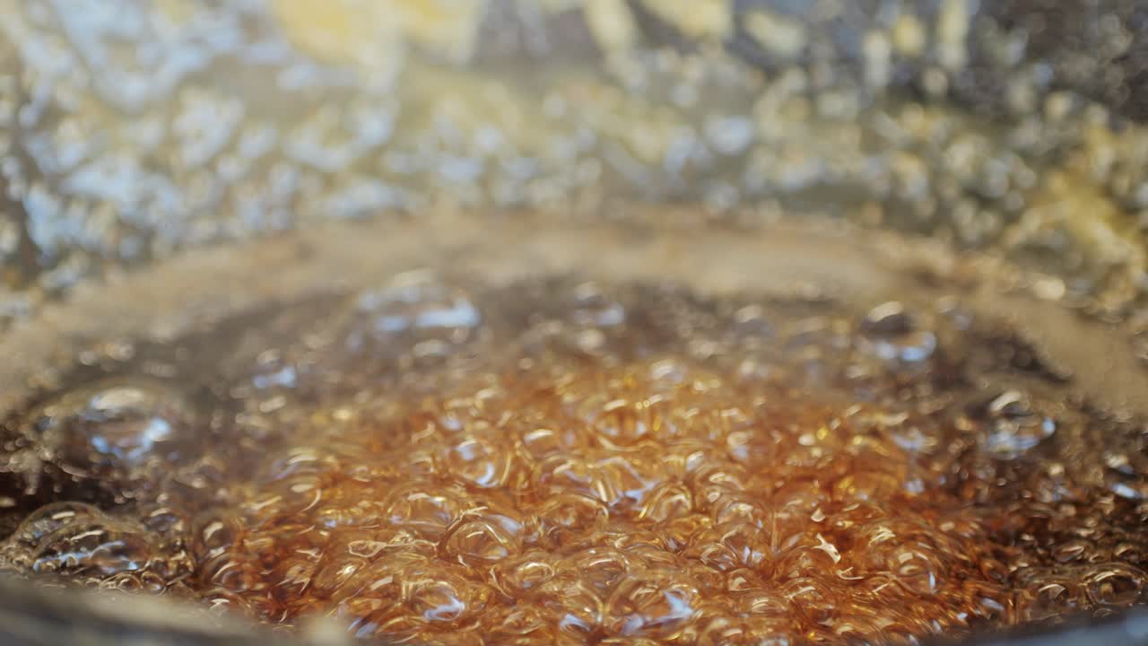 Close up of boiling sugar with bubbles turns into caramel in black pan, caramelization, chef cooking dessert in cafe, restaurant pastry food. Chinese winter sweet dessert Tanghulu. Fruits in sugar caramelized. Street food market concept