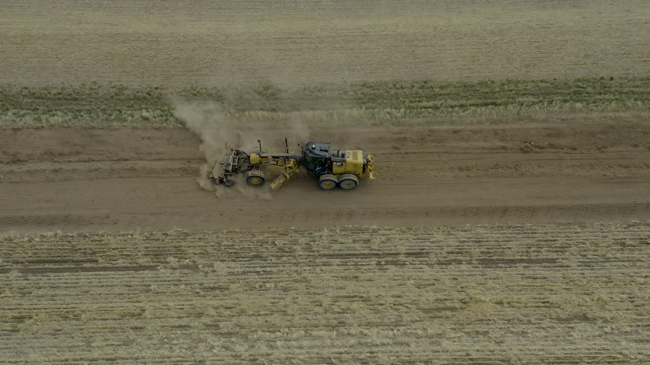 vista lateral aérea, motoniveladora de carreteras de tractor aplanando la superficie del campo para una nueva carretera, saskatchewan, canadá