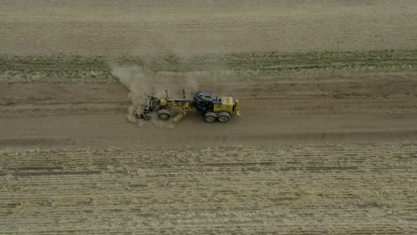 Vista-Lateral-Aérea,-Motoniveladora-De-Carreteras-De-Tractor-Aplanando-La-Superficie-Del-Campo-Para-Una-Nueva-Carretera,-Saskatchewan,-Canadá