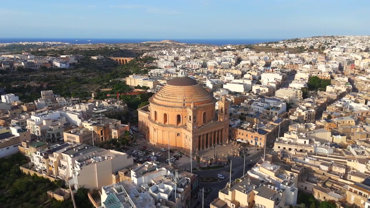 Vola in alto sopra l'iconica Chiesa di Mosta, rivelando la sua grande cupola e il bellissimo esterno, sullo sfondo dell'incantevole paesaggio di Malta in questo accattivante video con drone.