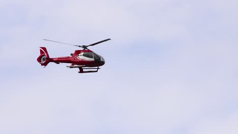 a red helicopter flies smoothly against a cloudy sky, showcasing aerial views near port campbell, victoria, australia