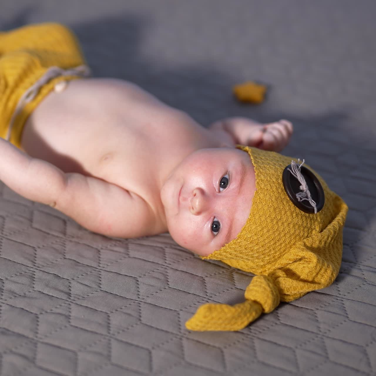 Nice little baby in yellow costume of gnome lies with his head to the camera. Baby in a hat with big button. Close up