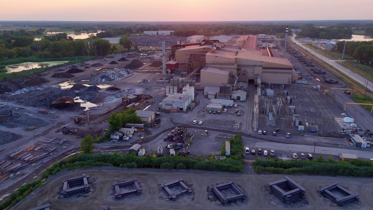 Vista aérea de uma usina industrial de reciclagem de aço em Monroe, Michigan, ao pôr do sol, com pilhas de vigas de aço