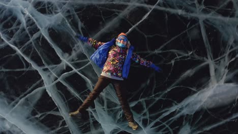 una niña en invierno yace en el hielo, agitando sus brazos y piernas hacia el lado, representando a un ángel