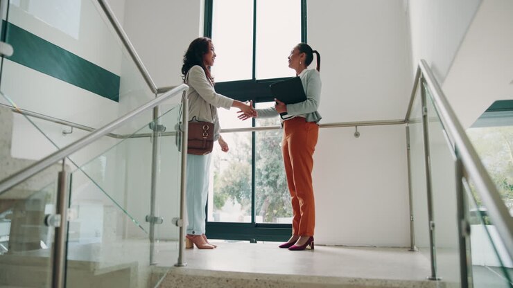 Two businesswomen shaking hands and discussing a business deal in an office building